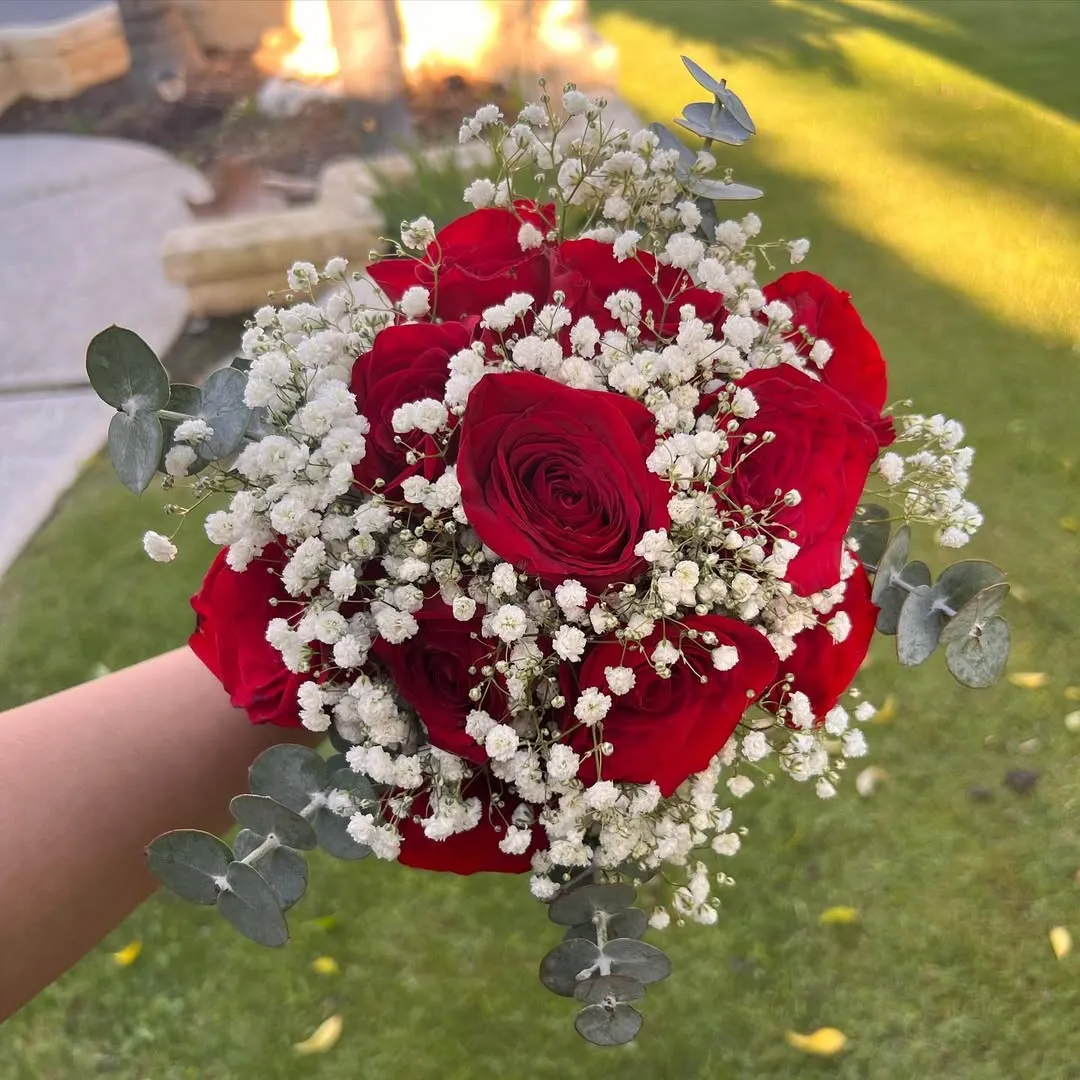 Hand holding a red rose bouquet with baby's breath and eucalyptus outdoors