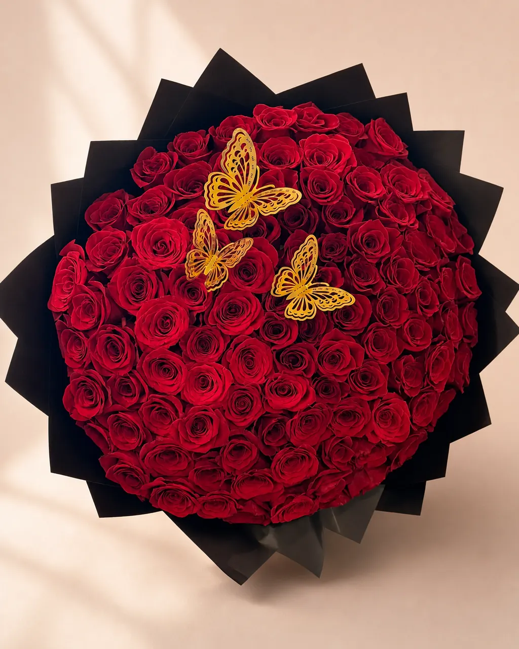 Monarch Night: one hundred red roses with gold butterflies in black wrap, on a blush backdrop